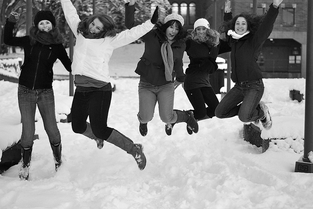 5 young students jumping for joy simultaneously in the snow in front of Old Main.